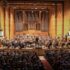 Ein Orchester mit großer Orgel im Hintergrund mit Publikum.